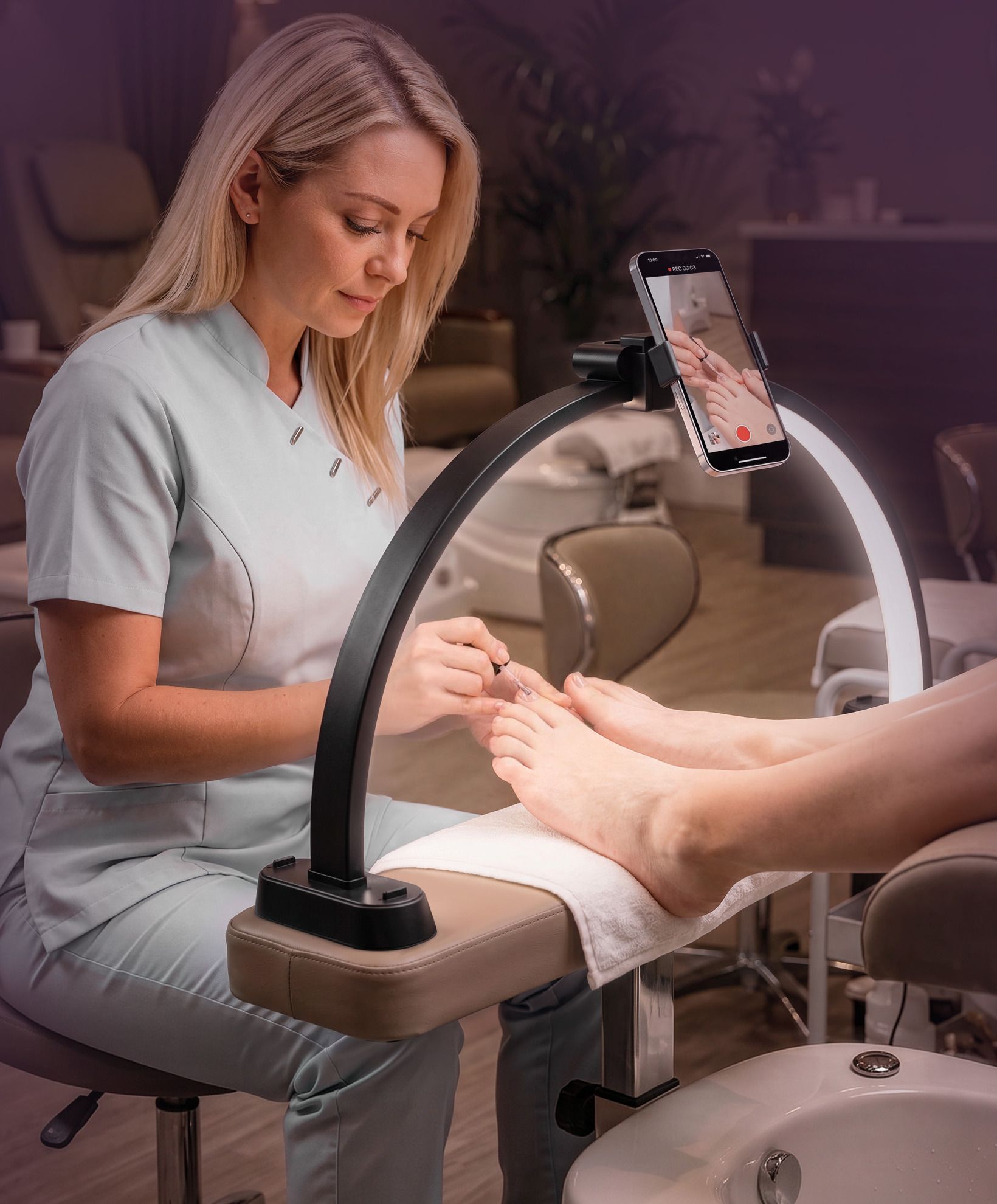 A technician gives a pedicure under the black Half-Moon Light, with a phone in the phone holder.