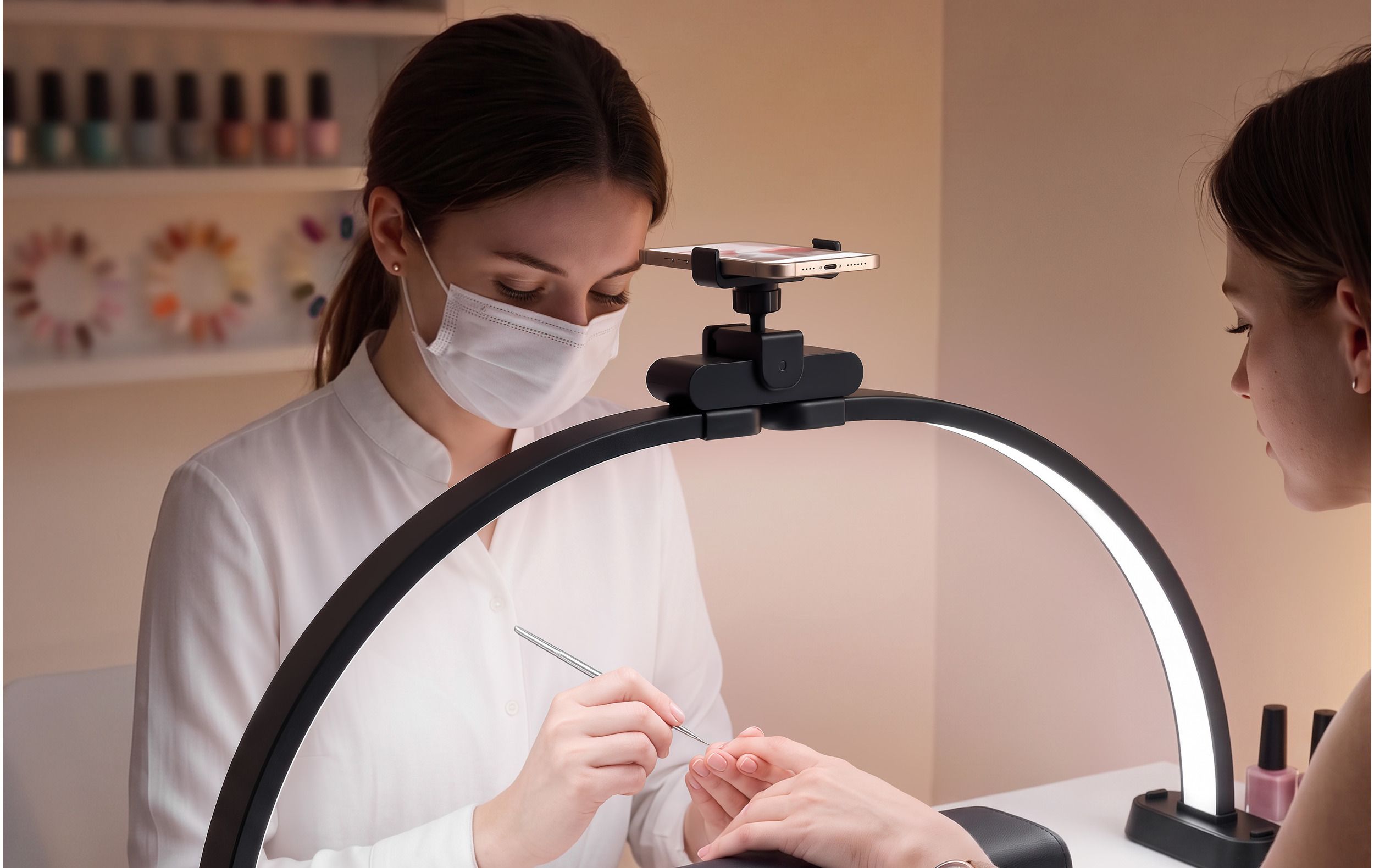 A nail technician works on a client's nails under the black Half-Moon Light, with a phone clipped into the holder above the control module.
