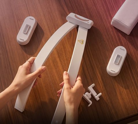 Hands unfold the light’s arms on a table, next to the two bases and the phone holder.