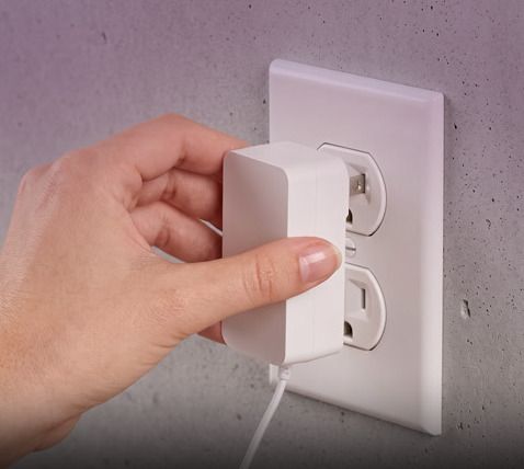 A hand plugs the power adapter into a wall outlet.